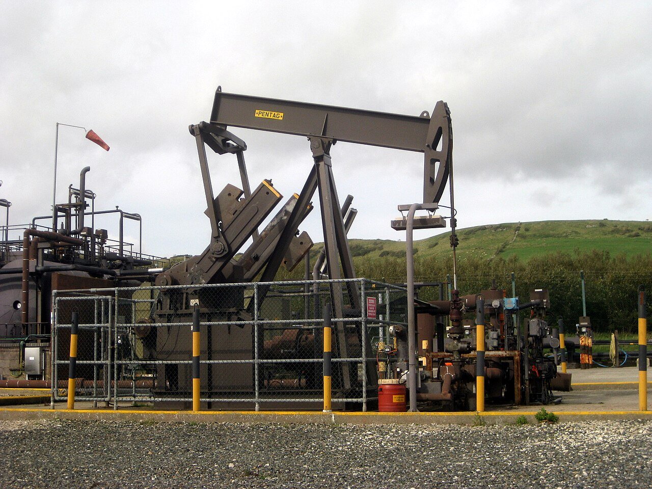 Surface pumping unit at an oil production site — upstream facilities introduce permit, gas monitoring and sour service requirements into the tender scope